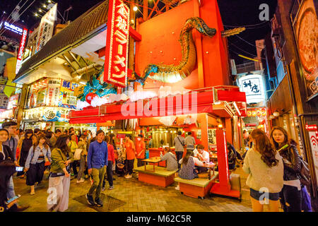 Osaka, Japan - April 29, 2017: tourists walk the streets of Namba District by night with various food signages. Namba is also known as an entertainment district with bars, restaurants and trendy shops Stock Photo