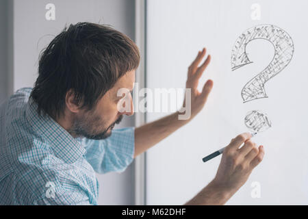 Perplexed businessman drawing question marks on whiteboard in the office, selective focus Stock Photo