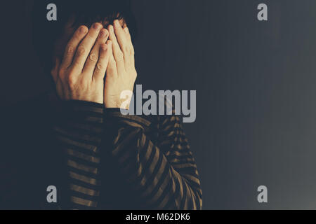 Desperate man crying alone, low key portrait with selective focus Stock Photo