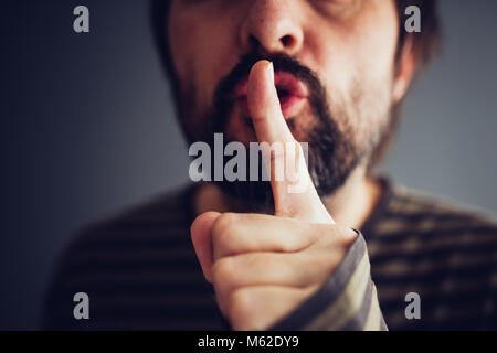 Man saying hush or be quiet with finger on lips, close up with selective focus Stock Photo