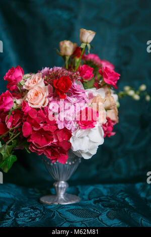 An asymmetric bouquet in a vase of roses, carnations and hydrangeas on a dark blue background Stock Photo