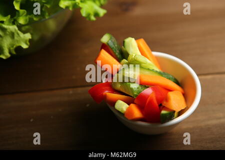 Pepper, carrots, celery, raw cucumber are cut into strips. On the plate. Next to it are lettuce leaves, basil. On a background of cloth, burlap, woode Stock Photo