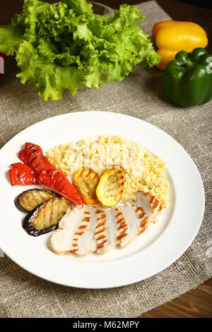 Grilled chicken with slices, with vegetables, bulgur on a white plate. In the background, lettuce leaves, color pepper. Low-calorie, dietary food for  Stock Photo