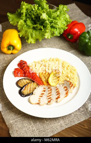 Grilled chicken with slices, with vegetables, bulgur on a white plate. In the background, lettuce leaves, color pepper. Low-calorie, dietary food for  Stock Photo