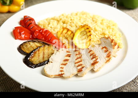 Grilled chicken with slices, with vegetables, bulgur on a white plate. In the background, lettuce leaves, color pepper. Low-calorie, dietary food for  Stock Photo