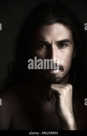 Handsome young man with serious expression and chin on hand, looking at camera, natural light Stock Photo