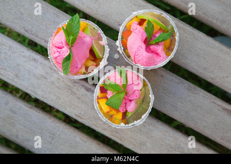 Three glasses with fruit salad and strawberry ice cream on the wooden surface. Top view Stock Photo