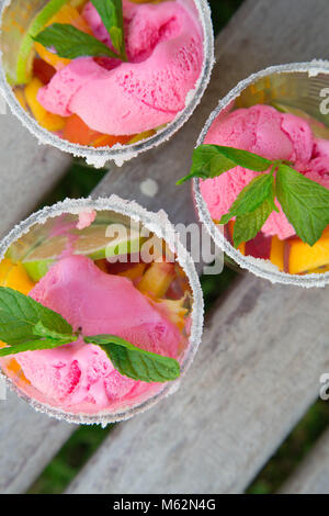 Three glasses with fruit salad and strawberry ice cream on the wooden surface. Top view Stock Photo