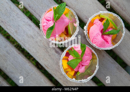 Three glasses with fruit salad and strawberry ice cream on the wooden surface. Free space for a text.Top view Stock Photo