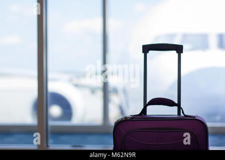Purple carry on luggage stands by boarding gate window with airplane blurred on the background outdoors. Business trip, travel concept Stock Photo