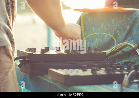 DJ playing music with professional equipment including laptop, console controller and power amplifier at sunset for beach party Stock Photo