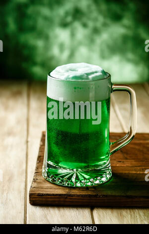 closeup of a glass jar with dyed green beer on a wooden rustic surface, against a green background with some blank space on top Stock Photo