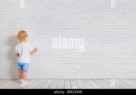 Baby boy with paint brush standing back near brick wall Stock Photo