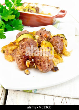 Meatballs baked with zucchini, cheese and nuts in a dish on a towel, parsley on a wooden board background Stock Photo