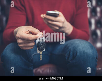 Close up on a man sitting on sofa with a smartphone and car keys Stock Photo