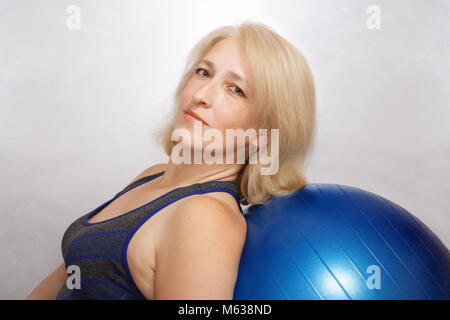 A middle-aged woman performs an exercise in Pilates, is leaned on fitball. Affordable sports at home Stock Photo