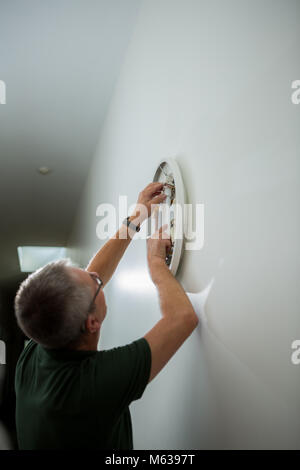 White handyman with grey hair repairs interior light Stock Photo