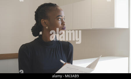 Side portrait of the african woman with natural make-up at the reception. Charming brunette is thoughtfully looking aside while holding the documents. Stock Photo