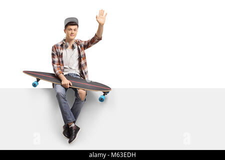 Teenage skater boy with a longboard sitting on a panel and waving isolated on white background Stock Photo