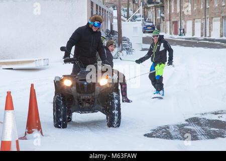 Men having fun with a quadbike pulling a snowboard through Seahouses village UK Stock Photo