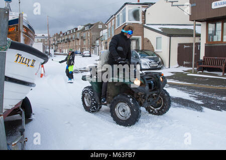 Men having fun with a quadbike pulling a snowboard through Seahouses village UK Stock Photo