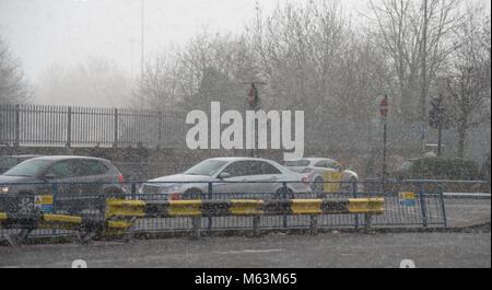 Merton, London, UK. 28 February 2018. After a day largely of strong winter sunshine a freshening east wind drives in snow in south west London to coincide with start of evening rush hour. Early evening traffic passes through Morden town centre in a snow shower. Credit: Malcolm Park/Alamy Live News. Stock Photo