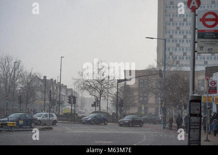 Merton, London, UK. 28 February 2018. After a day largely of strong winter sunshine a freshening east wind drives in snow in south west London to coincide with start of evening rush hour. Early evening traffic passes through Morden town centre in a snow shower. Credit: Malcolm Park/Alamy Live News. Stock Photo