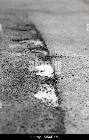 potholes forming on a road in line between new and old tarmac on street in the uk Stock Photo