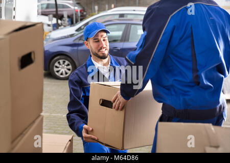 Close-up Of Two Happy Male Movers Holding Cardboard Box Stock Photo