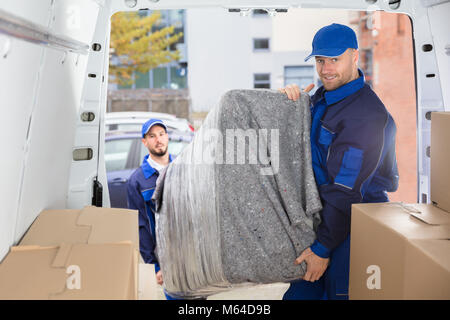 Two Happy Male Movers In Uniform Unloading Furniture From Truck Stock Photo