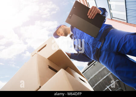 Low Section Of Young Male Worker Standing Near Cardboard Box Holding Clipboard Stock Photo