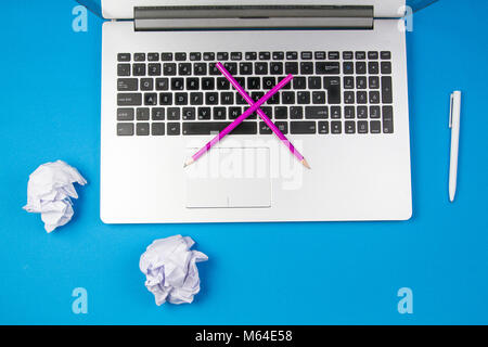 Laptop computer, cross pencils and crumpled paper on blue background Stock Photo
