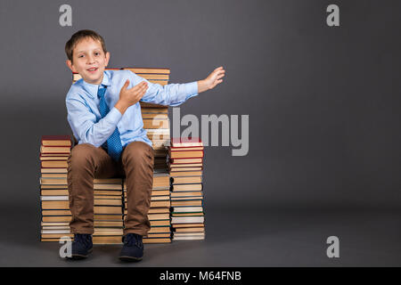 Education сoncept. Boy is leader sitting on a throne from books, demonstrates something behind himself. Copy space for the demonstration object Stock Photo