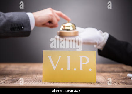Close-up Of Vip Card In Front Of Person Ringing Service Bell Held By Waiter Stock Photo