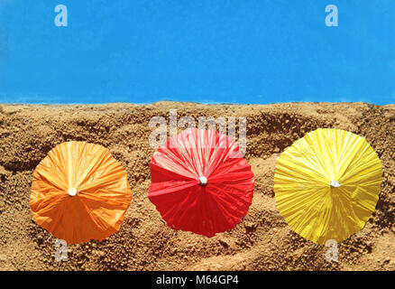 row of three colorful parasols at the beach, in the sand, blue water, top view Stock Photo