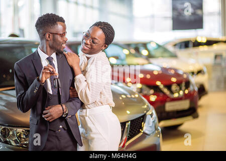 Visiting car dealership. couple holding key of their new car, looking at camera Stock Photo