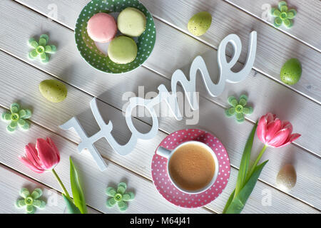 Spring coffee background. The word 'Home' made of wood, pink tulips, espresso, macarons and Spring decorations, top view. Stock Photo