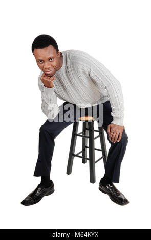 A full body image of a African American man in dress pants and sweater sitting on chair with his hand on the chin, isolated for white background Stock Photo