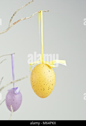 Yellow and purple decorative eggs hanging on dry branch. Abstract minimalism Easter decor concept, copy space Stock Photo