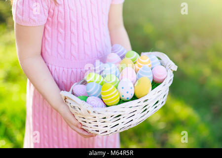 Easter egg hunt. Little girl with eggs basket. Kids searching for sweets and chocolate on Easter morning in garden. Child with spring pastel decoratio Stock Photo