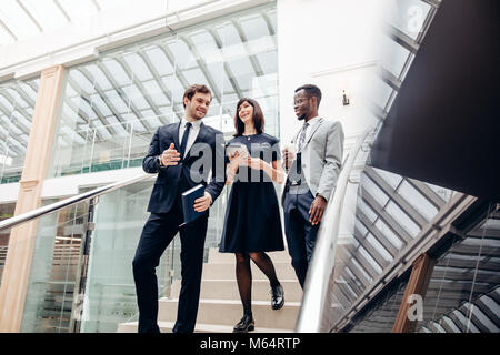 Three multiracial business people walking down on stairs with digital tablet Stock Photo