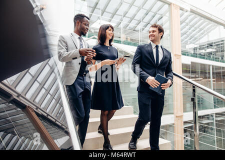 Three multiracial business people walking down on stairs with digital tablet Stock Photo