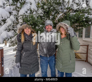 Three Young Adults Play In The Snow Behind A House As They Cover One Another And Cause Mischief With The Snow Stock Photo