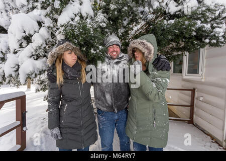 Three Young Adults Play In The Snow Behind A House As They Cover One Another And Cause Mischief With The Snow Stock Photo