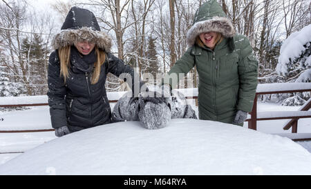 Two Yong Women In Winter Coats Playfully Push A Young Mans Face Into The Snow Stock Photo