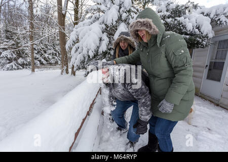 Two Yong Women In Winter Coats Playfully Push A Young Mans Face Into The Snow Stock Photo