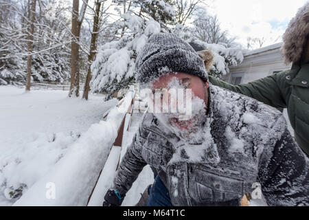 Two Yong Women In Winter Coats Playfully Push A Young Mans Face Into The Snow Stock Photo