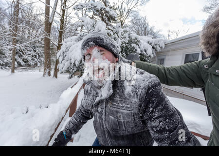 Two Yong Women In Winter Coats Playfully Push A Young Mans Face Into The Snow Stock Photo