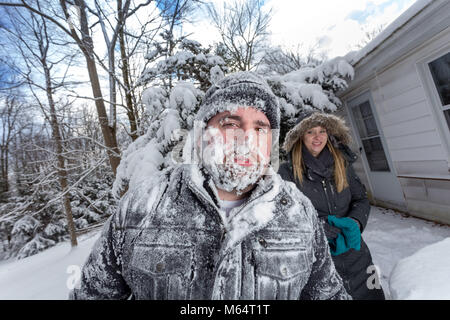 Two Yong Women In Winter Coats Playfully Push A Young Mans Face Into The Snow Stock Photo