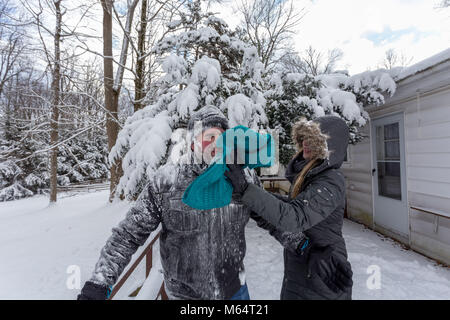 Two Yong Women In Winter Coats Playfully Push A Young Mans Face Into The Snow Stock Photo